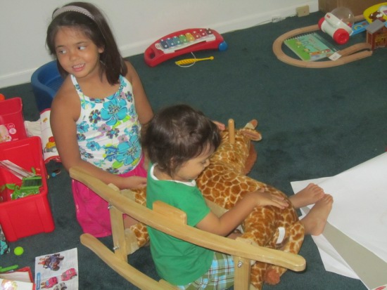 Yaya helps Adik get in this position with Rocky the Rocking Giraffe