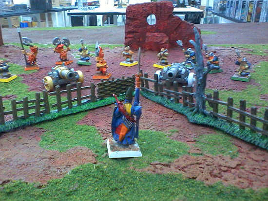 The High Elf poses on the table with other minis and terrain