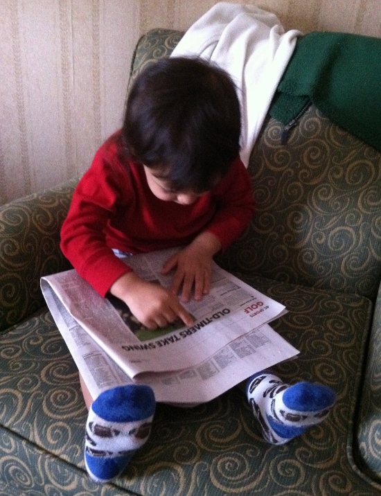 Reading the newspaper. Seriously. He's picking out words and reading them aloud